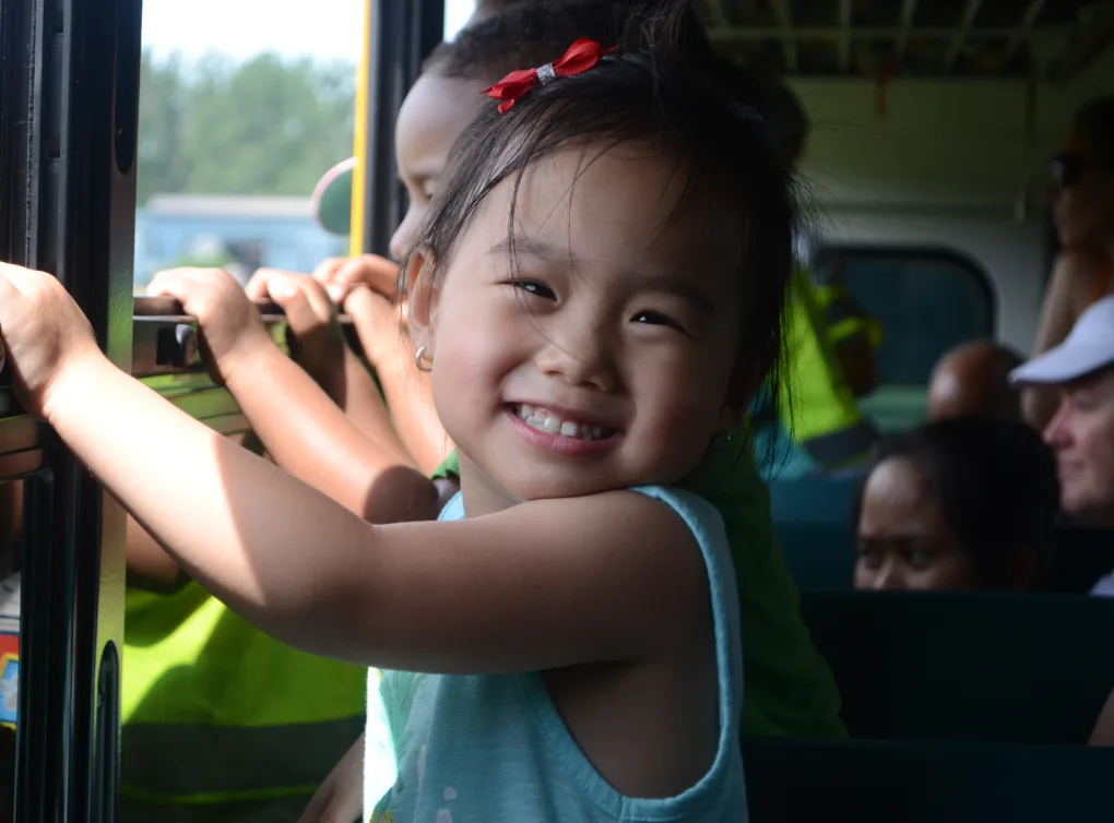 Petite fille en haut bleu tout sourire, agrippée à la barre d'un banc d'autobus