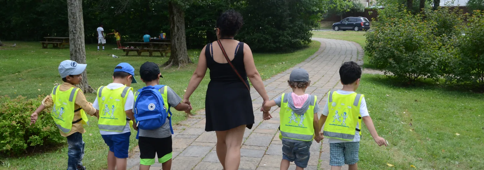 Éducatrice qui marche main dans la main avec cinq enfants en dossards sur un sentier