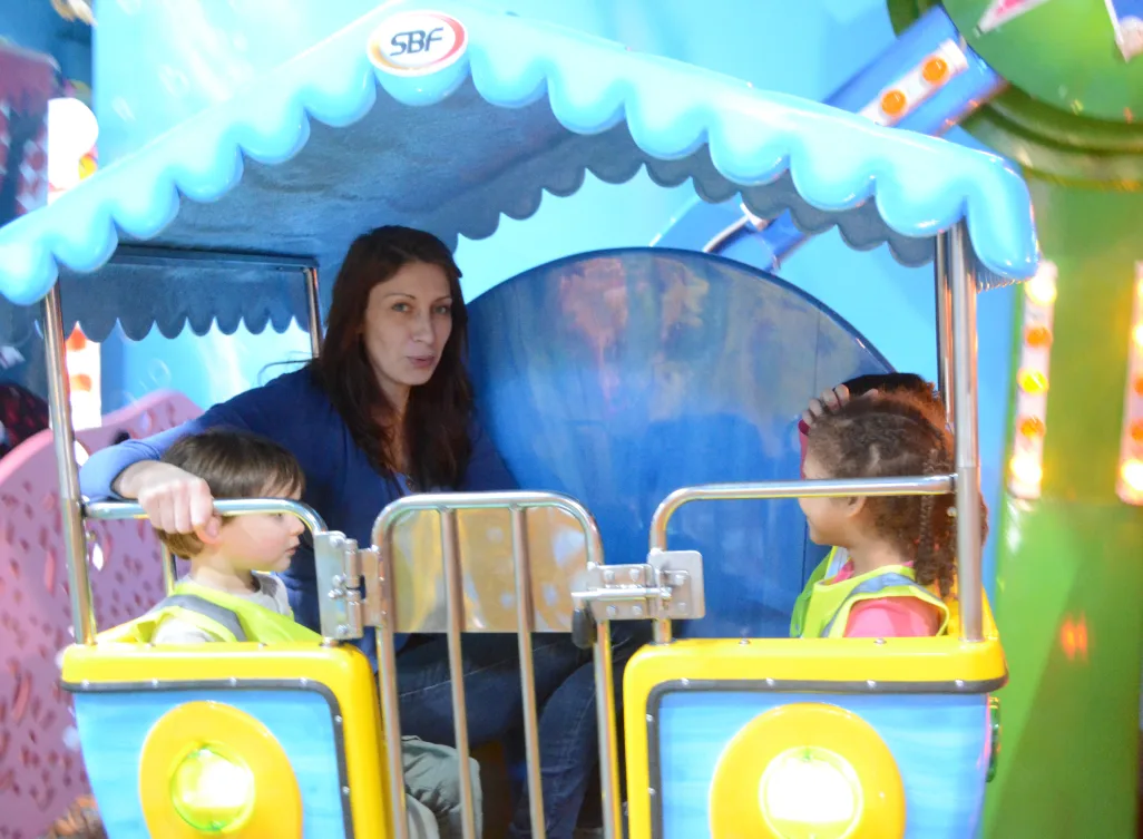 Une éducatrice à bord d'un petit train coloré avec deux tout-petits en dossards jaunes