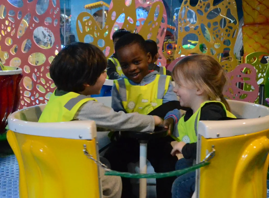 Trois enfants souriants en dossards jaunes qui partagent un manège tournant