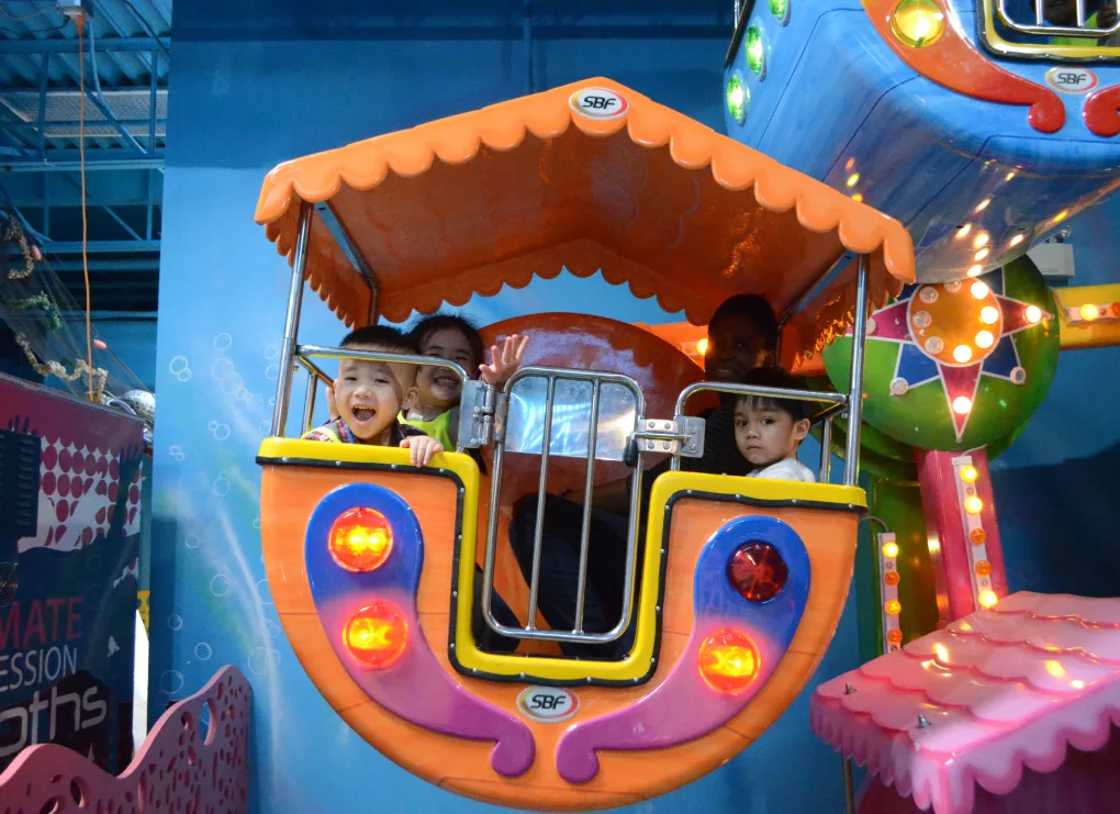 Des enfants regardent depuis une nacelle de grande roue illuminée et colorée