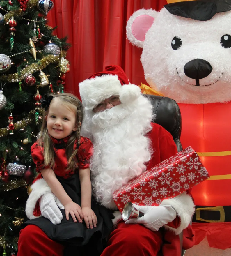 Fillette souriante en robe rouge assise avec le père Noël près du sapin décoré