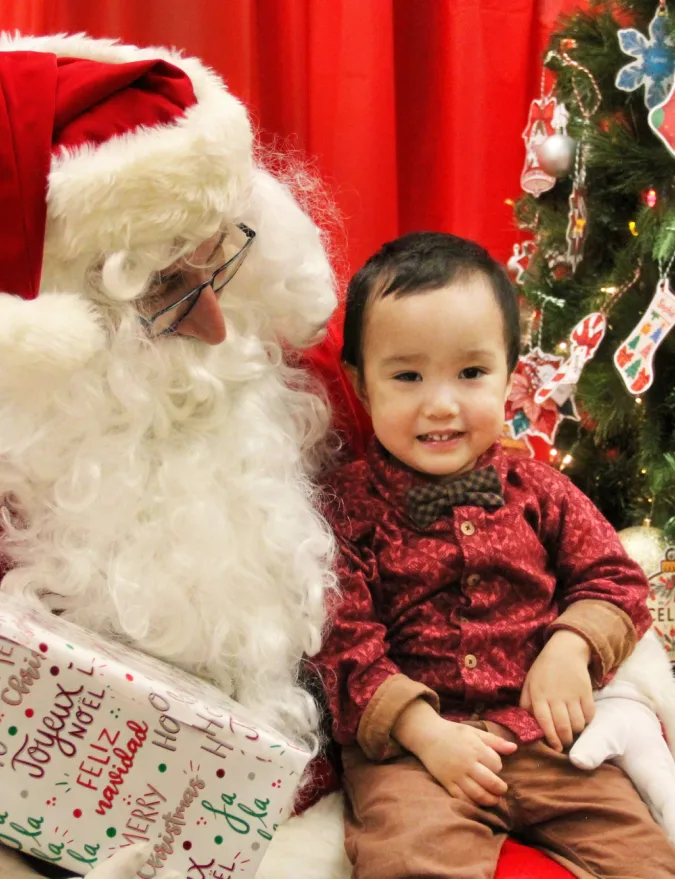Tout-petit en chandail rouge des fêtes assis sur les genoux du père Noël, un cadeau à ses côtés