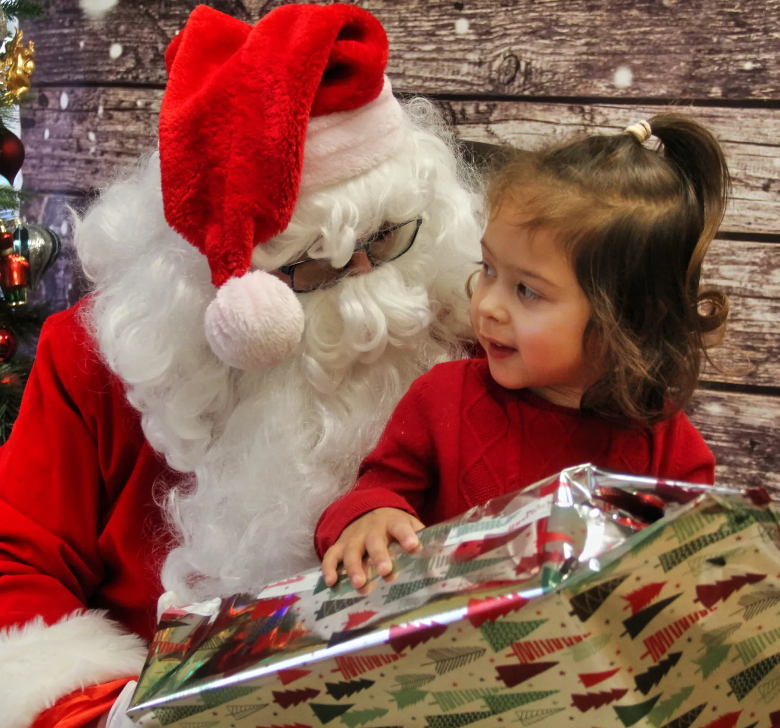 Père Noël et une fillette qui admirent un gros cadeau emballé de papier à motifs de sapins