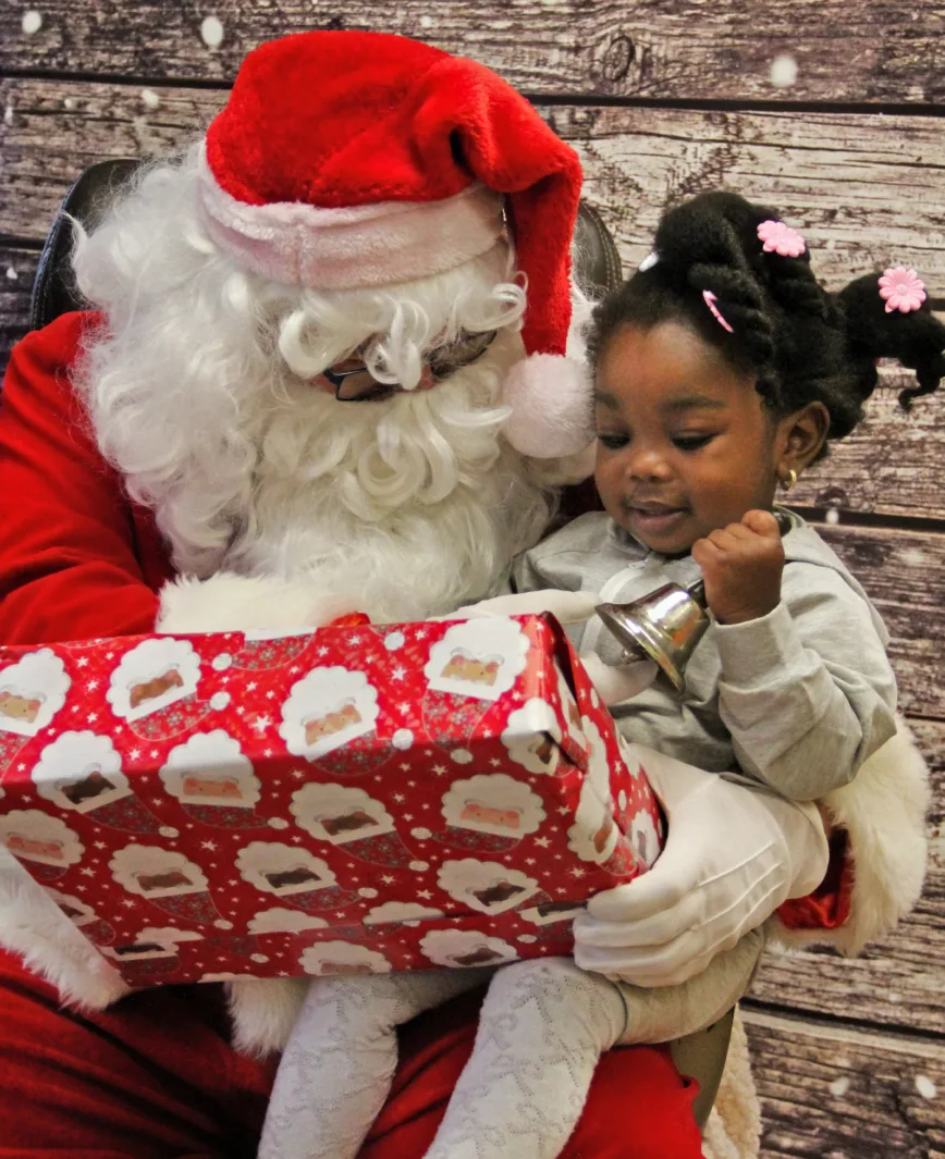 Bambine souriante sur les genoux du père Noël, tenant un cadeau au papier à motifs de pères Noël