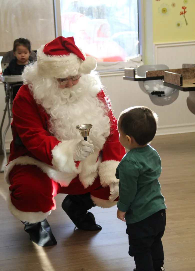 Le père Noël s'accroupit et fait tinter une clochette pour un tout-petit curieux