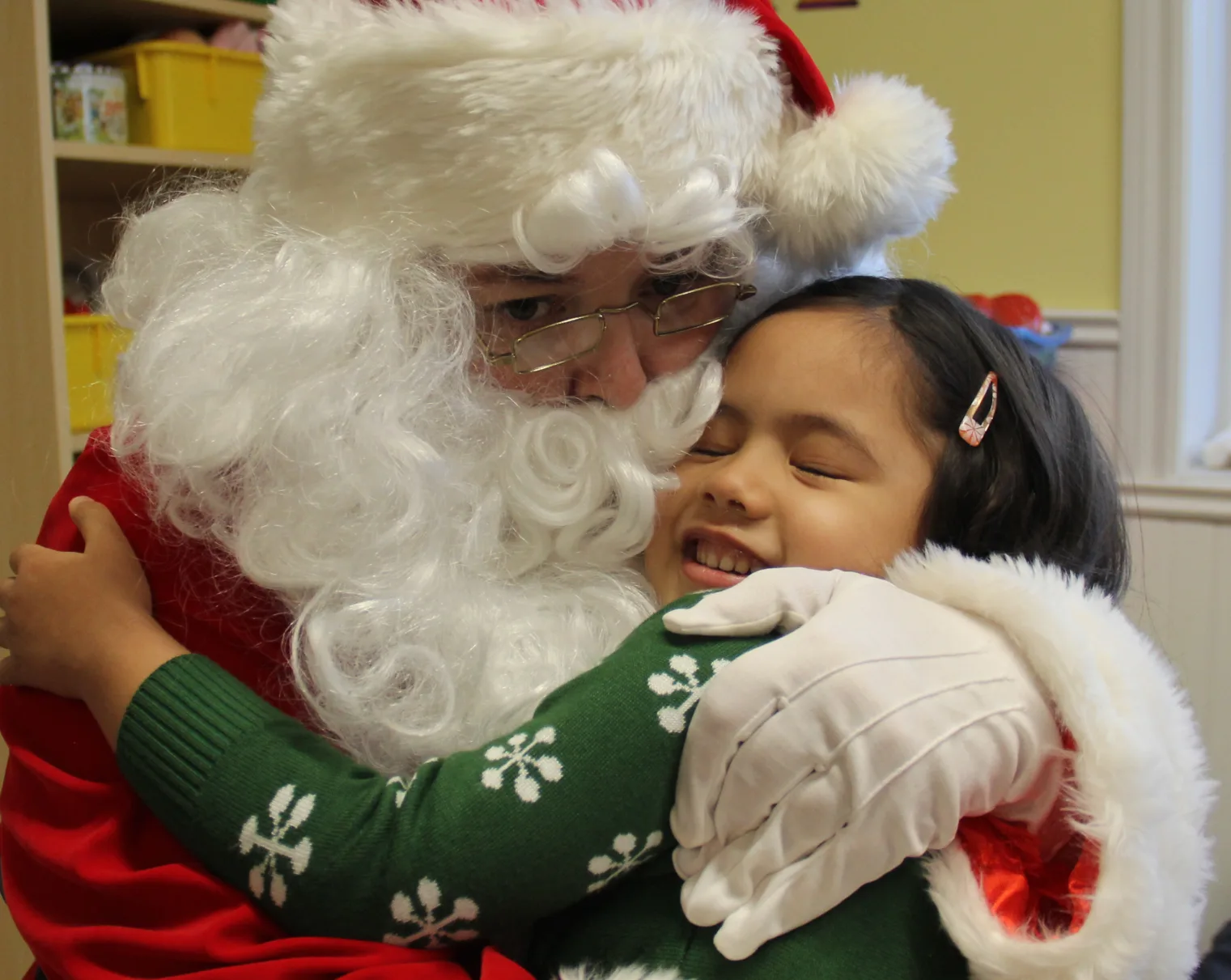 Une petite fille souriante en chandail des Fêtes reçoit un gros câlin du père Noël