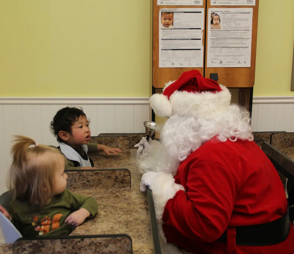 Le père Noël jase avec deux tout-petits assis à une table de la garderie
