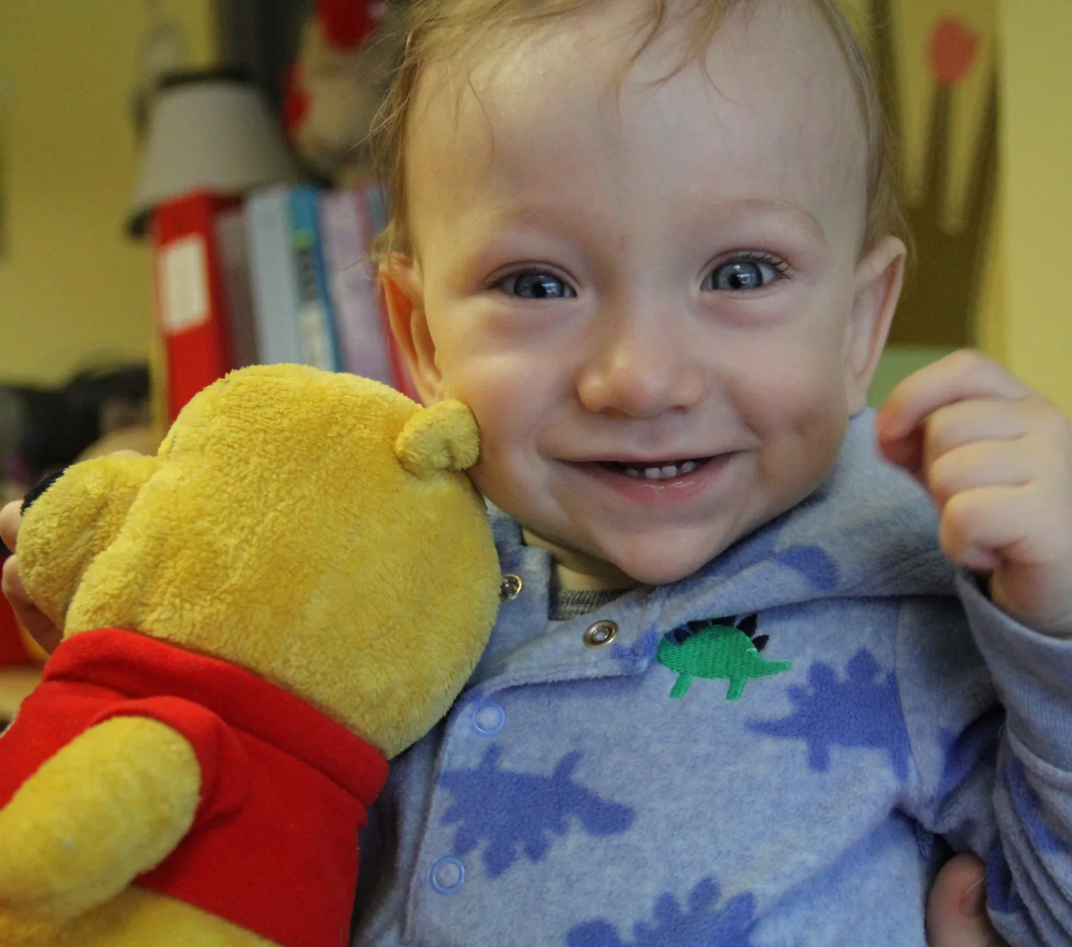 Bambin souriant en pyjama à dinosaures qui colle sa peluche Winnie l'ourson