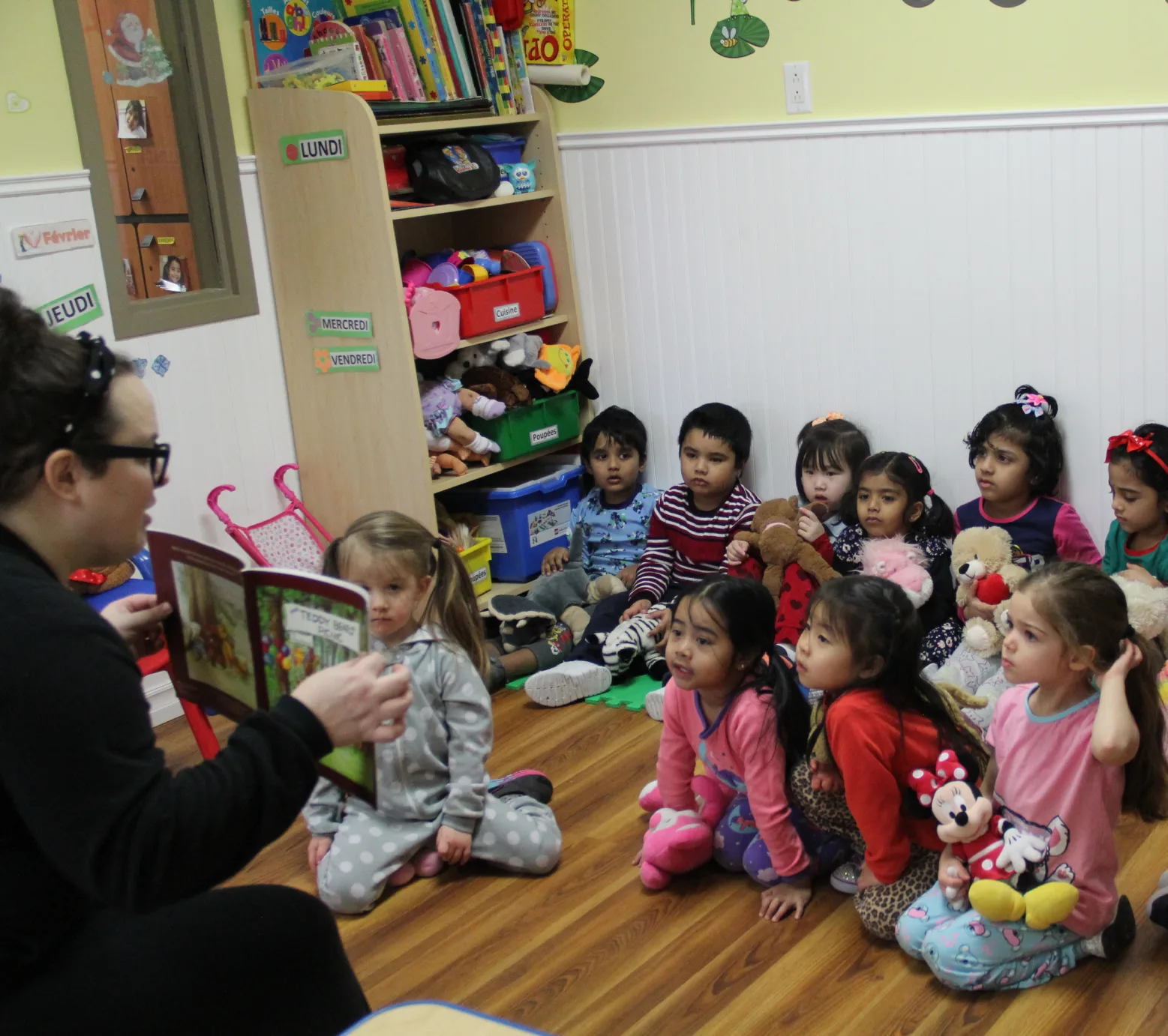 Éducatrice qui lit une histoire aux enfants assis par terre avec leurs toutous