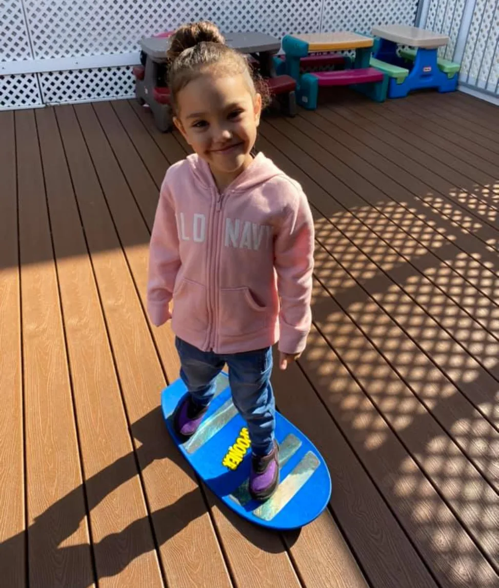 Enfant souriante en coton ouaté rose qui fait de l'équilibre sur une planche bleue dehors