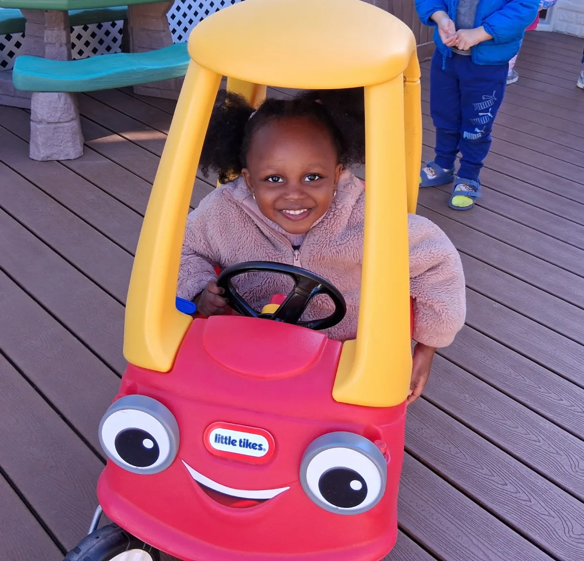 Bambine tout sourire au volant d'une petite auto rouge et jaune