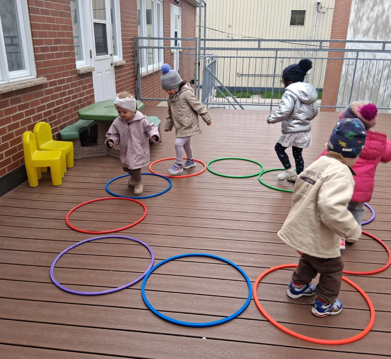 Enfants en habits d'hiver qui sautent dans des cerceaux colorés posés sur la terrasse