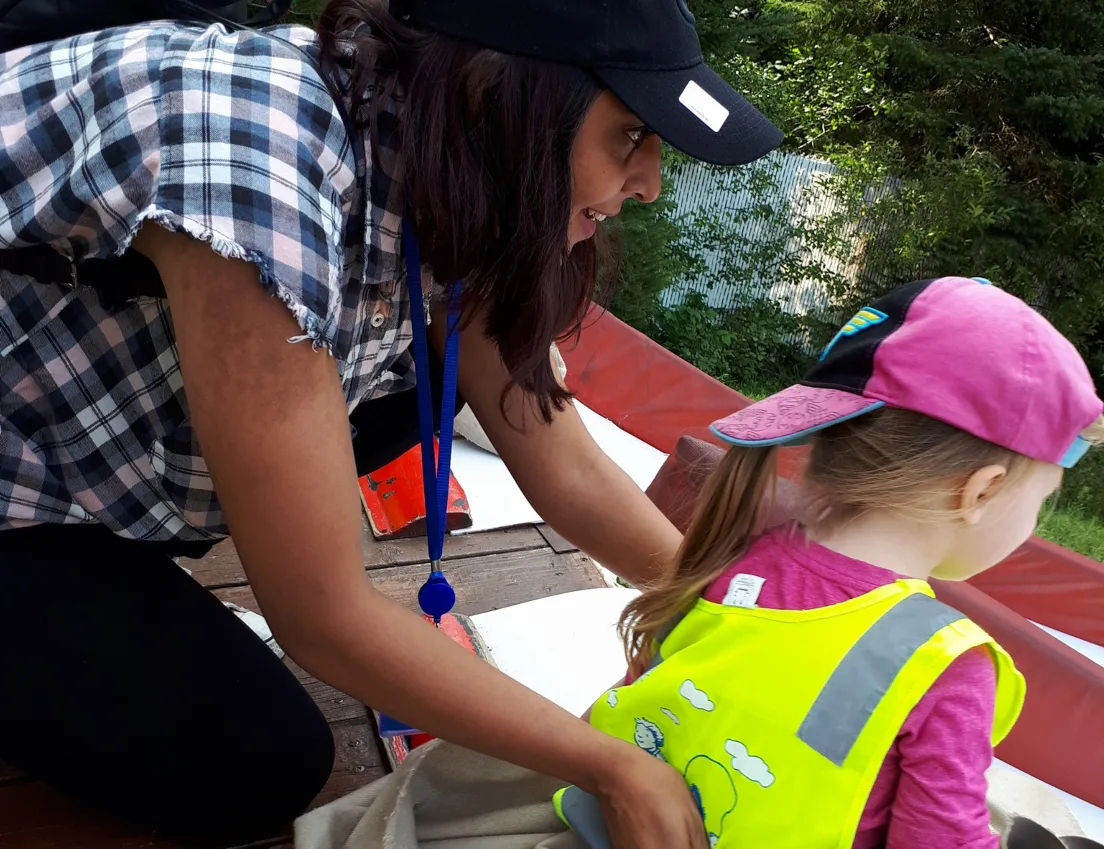 Une éducatrice aide une fillette qui porte une casquette rose et un dossard jaune