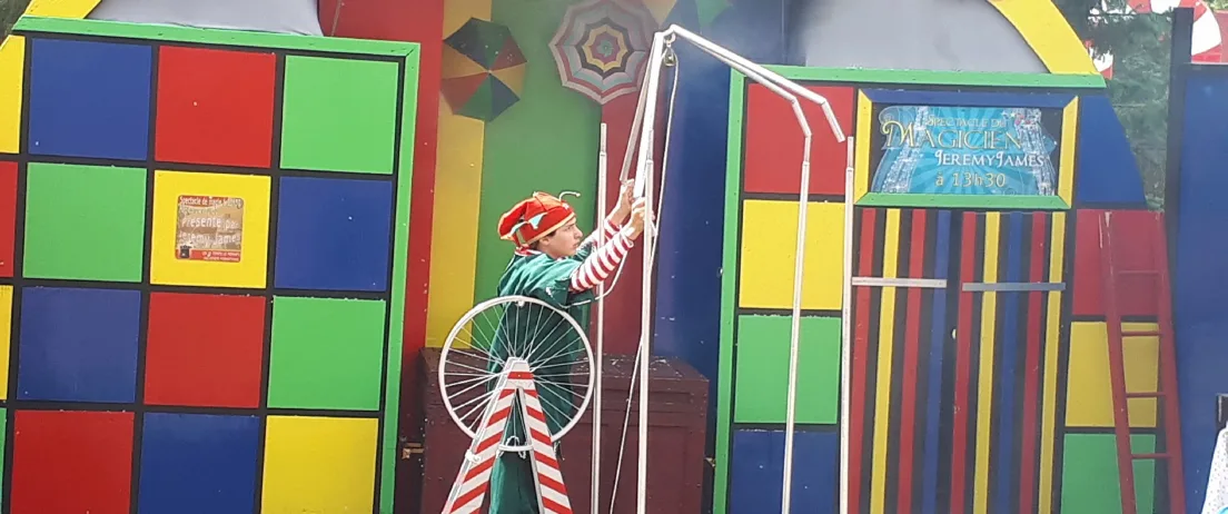 Un lutin acrobate en équilibre sur un monocycle au-dessus d'une scène colorée
