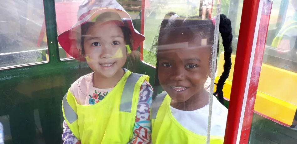 Deux enfants souriants en dossards jaunes assis ensemble dans un manège