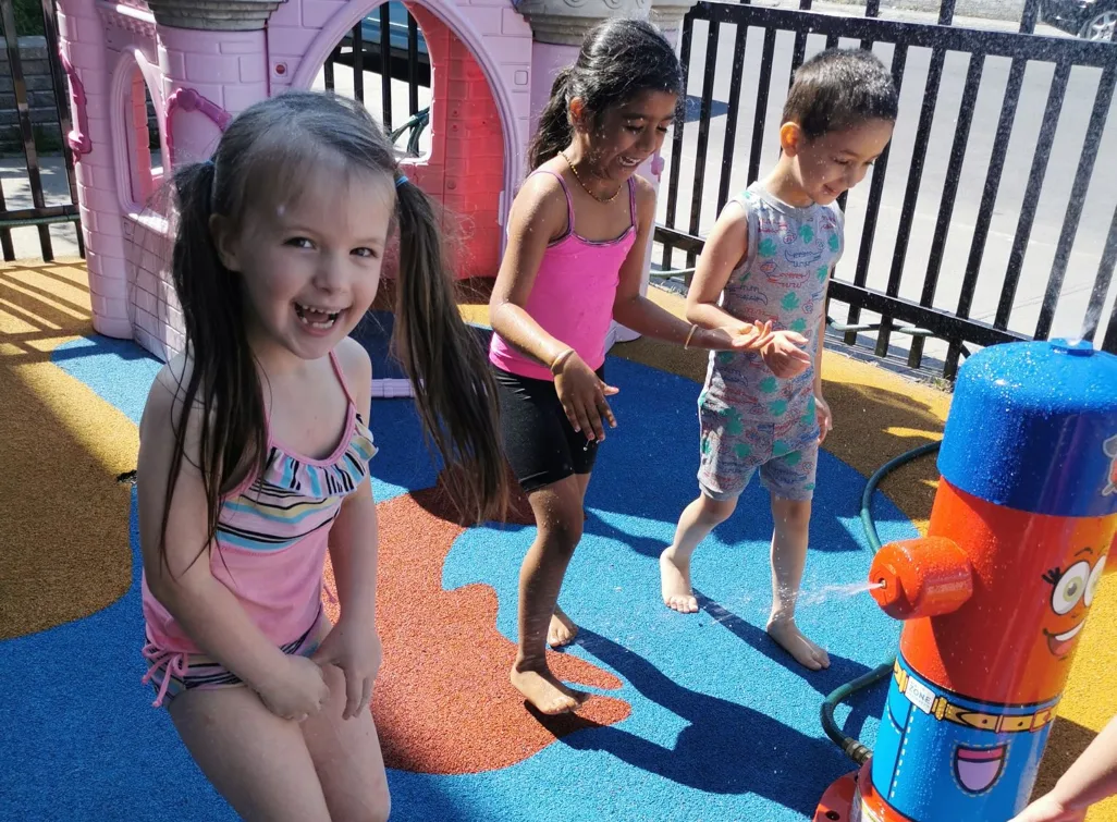 Trois fillettes souriantes qui jouent près de la borne-fontaine arrosoir sur la surface bleue