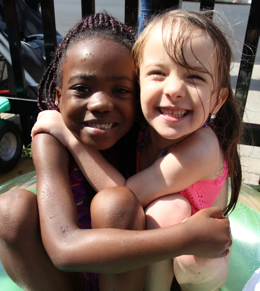 Deux fillettes souriantes qui se font un câlin dans la petite piscine au soleil