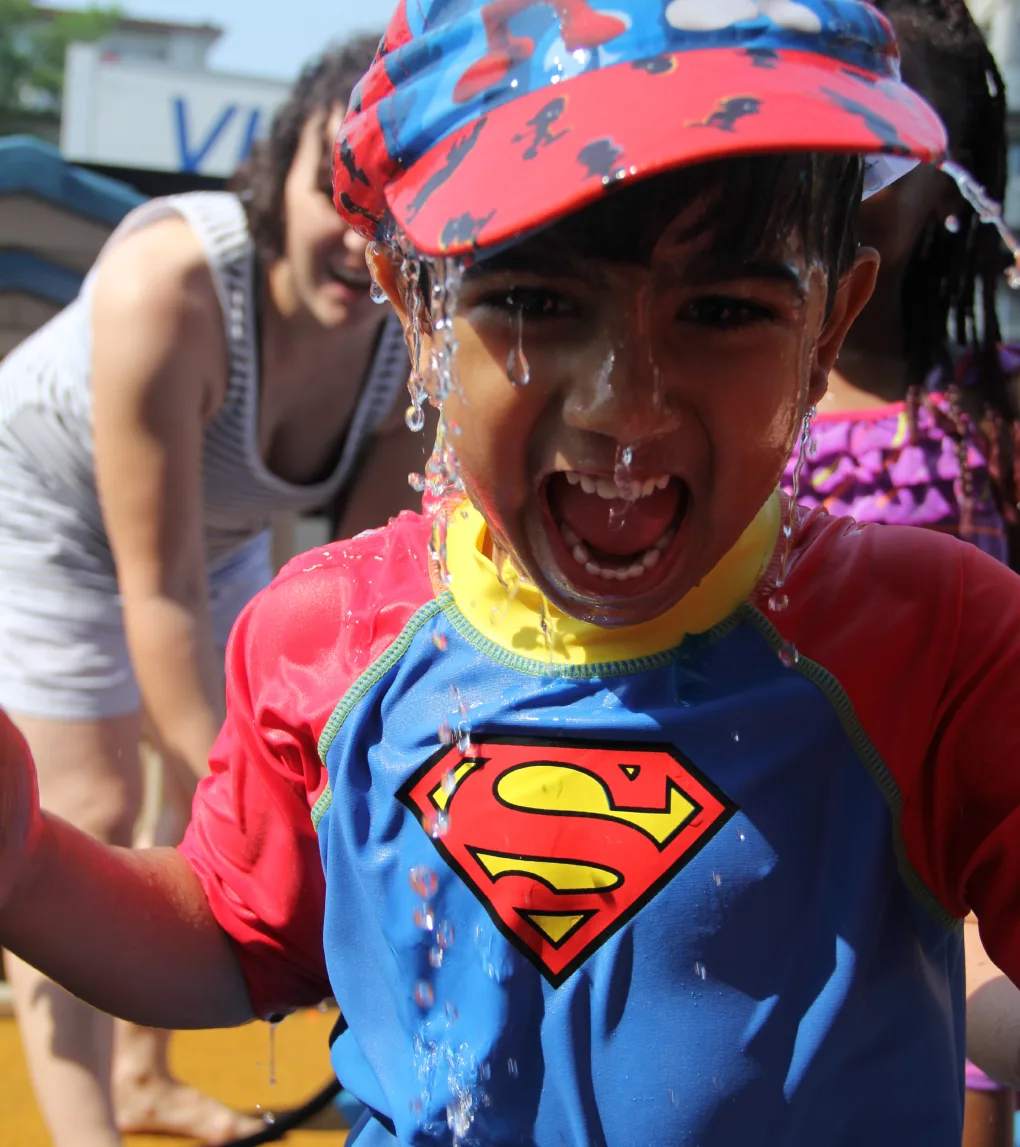 Un petit garçon en chandail de bain Superman qui rit en se faisant arroser