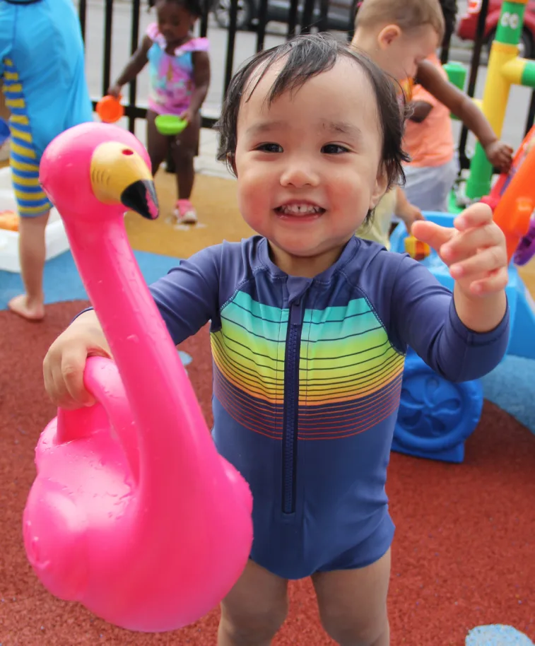 Bambin souriant en maillot arc-en-ciel qui transporte un flamant rose aux jeux d'eau